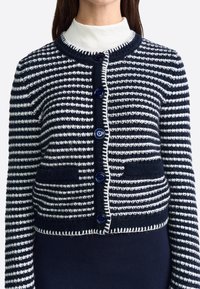 Cardigan a righe blu navy e bianche realizzato in maglia, con scollo rotondo, quattro bottoni blu e due tasche anteriori con bordi a contrasto.