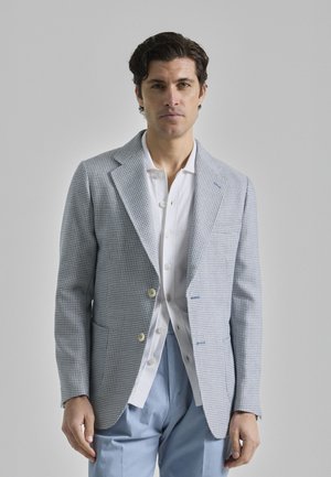 Blazer a cuadros en azul claro con solapas tipo muesca, dos botones y un bolsillo en el pecho, llevado sobre una camisa blanca y pantalones en azul claro.