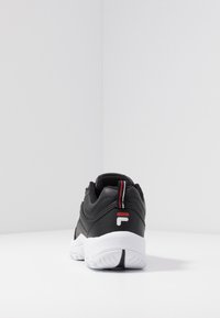 Zapatilla deportiva negra con cuello acolchado, parte superior de cuero texturizado, suela blanca y detalle en rojo en el talón y el logo.