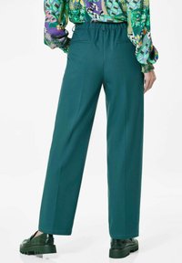 Teal wijde broek met een elastische tailleband, twee achterzakken en een gladde textuur, gecombineerd met donkergroene platform schoenen.