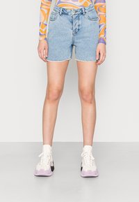 Vaaleansiniset farkkushortsit, joissa on repaleinen helma, klassinen viisi-taskumalli ja yhdistettynä valkoisiin ja vaaleanpunaisten tennareiden kanssa.