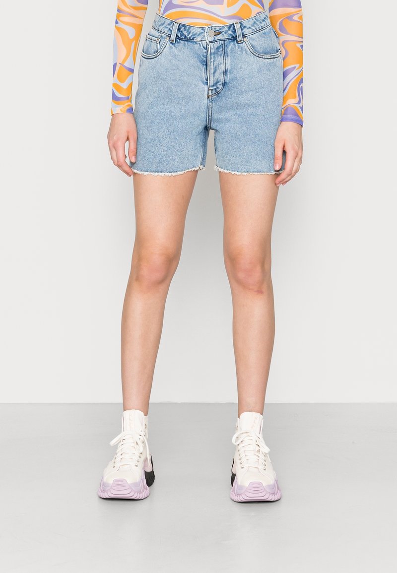 Vaaleansiniset farkkushortsit, joissa on repaleinen helma, klassinen viisi-taskumalli ja yhdistettynä valkoisiin ja vaaleanpunaisten tennareiden kanssa.