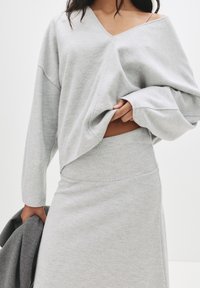 Pull overdimensionné gris clair avec un col en V et des manches longues, associé à une jupe grise assortie. Texture douce et silhouette simple.