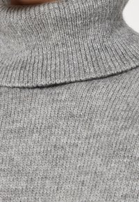 Maglione grigio a collo alto lavorato a maglia con una texture a coste e un colletto alto, che offre un aspetto morbido e una vestibilità accogliente.