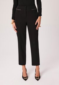 Czarne spodni o dopasowanym kroju z prostą nogawką, z dwoma bocznymi kieszeniami z metalowymi akcentami, w połączeniu z czarnymi szpilkami.