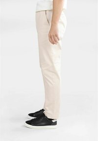Beige bomullbyxor med slim fit, med framfickor och sidofickor, i kombination med svarta sneakers med vita sulor.