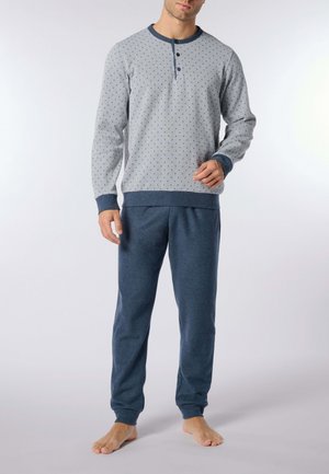 Maglia grigia a maniche lunghe con pois blu e chiusura a bottoni, abbinata a pantaloni della tuta blu scuro, con polsini e vita a coste.