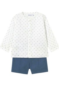 Camisa blanca de manga larga con patrón de puntos azules y cierre de botones, combinada con pantalones cortos azul marino con pliegues delanteros.