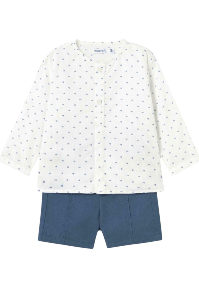 Camisa blanca de manga larga con patrón de puntos azules y cierre de botones, combinada con pantalones cortos azul marino con pliegues delanteros.