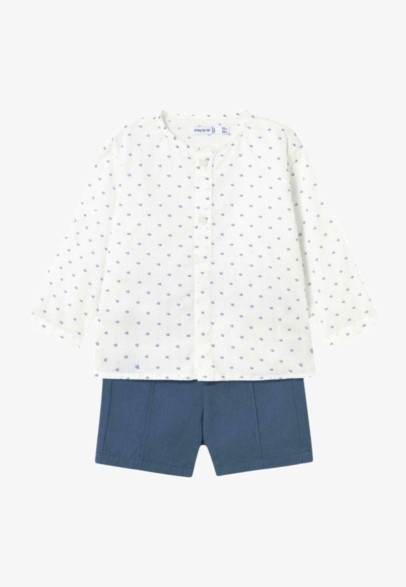 Camisa blanca de manga larga con patrón de puntos azules y cierre de botones, combinada con pantalones cortos azul marino con pliegues delanteros.
