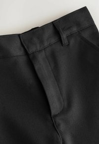 Schwarze Stoffhosen mit flachem Frontschnitt, Reißverschluss und gesteppten Nähten. Glatte Textur mit einem sauberen, maßgeschneiderten Design.