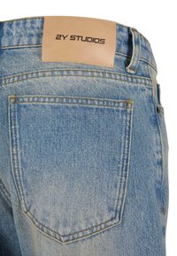 Helle blaue Jeans aus Denim verfügen über eine Gesäßtasche, sichtbare Nähte und ein hellbraunes Lederetikett mit der Prägung "2Y STUDIOS".