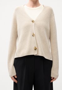 Beige gestrickte Strickjacke mit V-Ausschnitt, drei großen Knöpfen vorne und langen Ärmeln, mit lockerem Schnitt und gerippter Struktur.