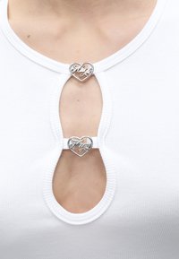 Λευκή ριμπ τοπ με λαιμόκοψη σε σχήμα κλειδιού, στερεωμένη με δύο ασημένια κλιπ σε σχήμα καρδιάς, χαραγμένα με τα γράμματα "Fay".