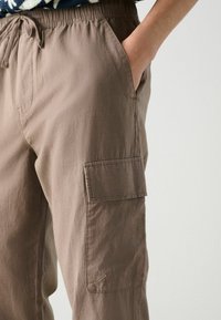 Cargo-Hosen aus weichem braunem Stoff, mit einem elastischen Bund, Seiten Taschen und einer aufgenähten Tasche über dem Knie. Glatte Textur, lässige Passform.