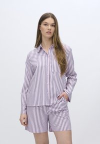 Pigiama a righe in rosa chiaro e navy. Maglietta a maniche lunghe con chiusura a bottoni e tasca; pantaloni corti con righe coordinate. Materiale morbido.