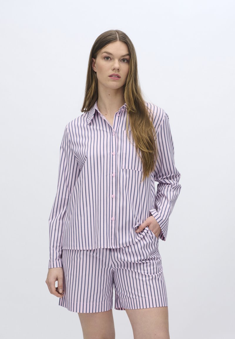 Pigiama a righe in rosa chiaro e navy. Maglietta a maniche lunghe con chiusura a bottoni e tasca; pantaloni corti con righe coordinate. Materiale morbido.
