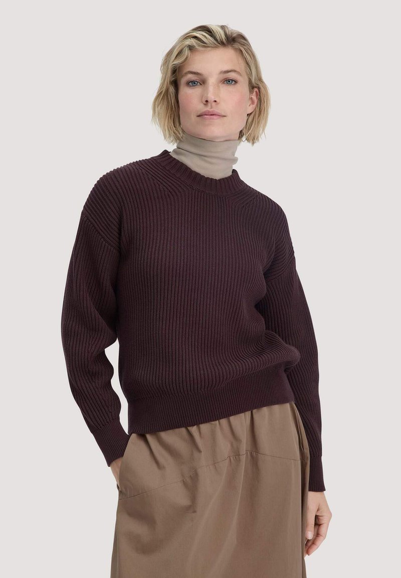 Bordeauxfarbener Rippstrickpullover mit Rundhalsausschnitt und lockeren Ärmeln. Über einem beigen Rollkragenpullover getragen, kombiniert mit einem braunen Rock.