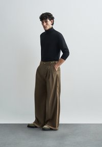 Zwarte coltrui, loszittende bruine broek met plooien, zijstreep en een ontspannen ontwerp. Schoeisel met een chunky zool.