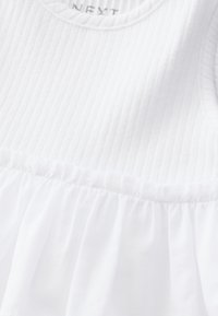 White garment featuring a textured, ribbed top section and a smooth, gathered bottom. Label reads "NEXT." Soft fabric.