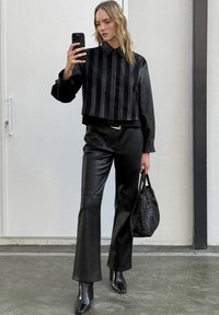 Obcisła czarna bluzka z pionowymi satynowymi paskami, zestawiona z dopasowanymi czarnymi skórzanymi spodniami. Dodatki obejmują fakturowaną czarną torebkę oraz botki na obcasie.