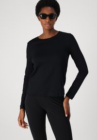 Zwart langshirt met ronde halslijn, gemaakt van zacht materiaal. Gecombineerd met zwarte leggings en aangevuld met hoekige zwarte zonnebril.