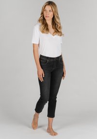 Schwarze Jeans aus Denim mit mittelhohem Bund, schmaler Passform und cropped Länge, kombiniert mit einem kurzärmeligen weißen V-Ausschnitt-T-Shirt.