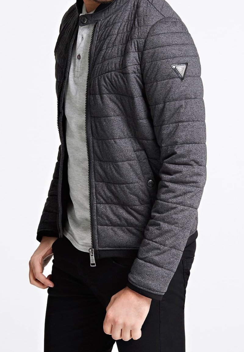 Quiltemed grå bomberjakke med ståkrave, frontlynlås og sort kant. Den har et elegant design og sidelommer som accent.