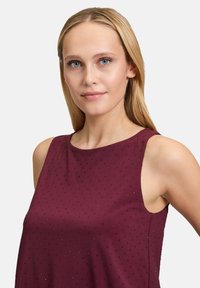 Top senza maniche in color bordeaux con una vestibilità rilassata, caratterizzato da piccoli puntini decorativi su tutta la superficie del tessuto e da una texture liscia e morbida.