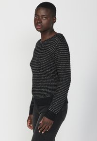 Maglione lavorato a maglia nero e argento con un motivo testurizzato, scollatura rotonda e polsini e orlo a costine. Abbinato a jeans scuri.
