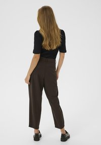 Pantaloni maro cu talie înaltă, cu o croială lejeră și buzunare laterale, asortați cu un top negru cu mânecă scurtă, văzuți din spate.