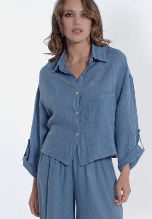 Camicia in lino azzurro chiaro con vestibilità rilassata, chiusura con bottoni e taschino singolo sul petto. Caratterizzata da maniche arrotolate con bottoni.