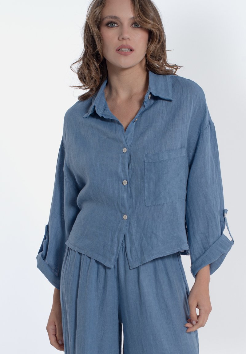 Camicia in lino azzurro chiaro con vestibilità rilassata, chiusura con bottoni e taschino singolo sul petto. Caratterizzata da maniche arrotolate con bottoni. 