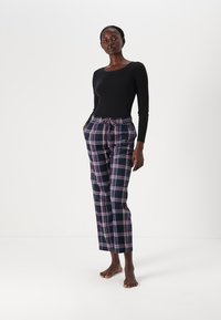 Haut à manches longues noir associé à un pantalon à cordon écossais dans les tons bleu marine, rose et blanc. Le pantalon présente une coupe décontractée et une longueur de cheville.