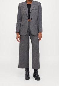 Grå rutig kavaj med notch-lapper och enkel knappstängning, ihop med matchande vida byxor och svarta klackboots.