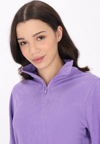 Pullover in pile viola con colletto a mezza zip, caratterizzato da una texture morbida e una vestibilità aderente. Ideale per stratificare in ambienti più freschi.