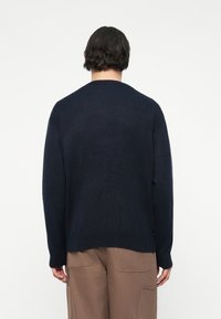 Pulover tricotat de culoare bleumarin, cu un croi lejer, manșete și tiv din material întărit, cu guler rotund și detalii de cusătură minime, văzut din spate.