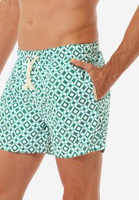 Pantaloni da bagno verdi con un motivo geometrico bianco e teal, vita elastica con cordino e tasche laterali.