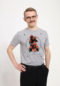 Camiseta de algodón gris con un gráfico floral que presenta flores rojas y negras, acentuado por contornos negros y texto alrededor del diseño.