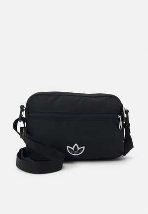 Sac bandoulière rectangulaire noir avec poche avant zippée, sangle réglable et logo trèfle blanc au centre devant.