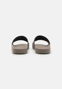 Zijslippers met een zwarte bovenband en een gestructureerde bruine zool. Plat ontwerp en open tenen. Heeft een minimalistische stijl en duurzaam materiaal.