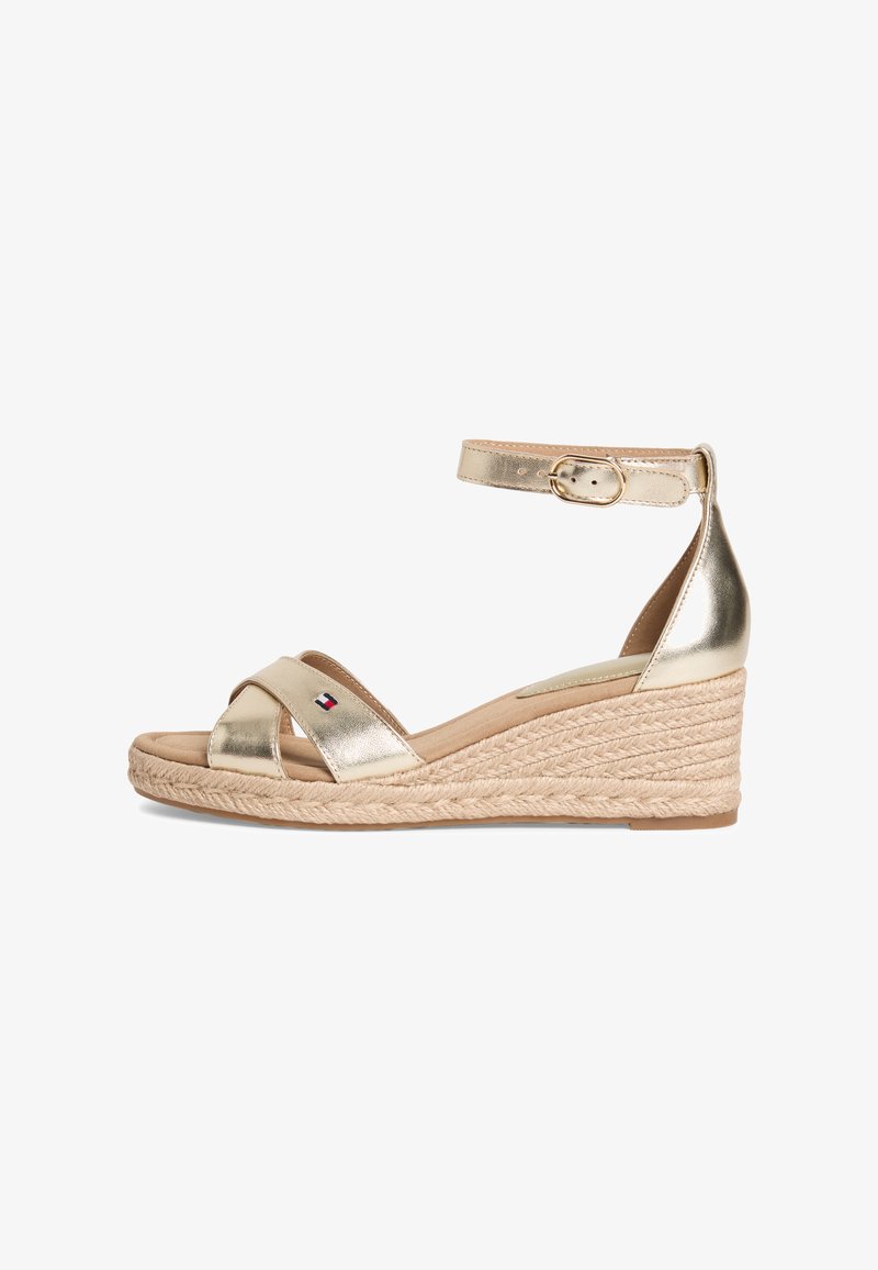 Χρυσαφί μεταλλικό σανδάλι πλατφόρμα με λουρί στον αστράγαλο και αγκράφα, πλεγμένη σόλα από τζούτ και μικρό λογότυπο σημαίας στο μπροστινό λουρί.