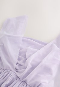 Tissu léger violet clair transparent avec des plis doux et des fronces sur un fond lisse et clair.