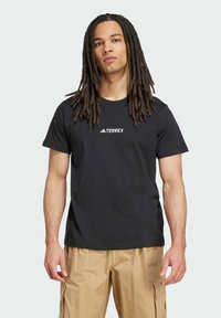 Camiseta de manga corta negra con un logo blanco de "TERREX" en la parte delantera. La tela parece suave y tiene un ajuste clásico.
