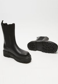 Black leather ankle boots with elastic side panels, a chunky platform sole, and textured rubber outsole for traction. Rounded toe design.