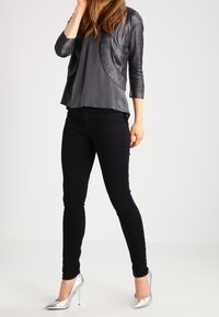 Vaqueros negros ajustados combinados con una blusa de satén gris oscuro y un cárdigan plateado brillante. Unos tacones altos plateados complementan el conjunto.