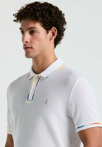Witte poloshirt met een textuurstof, voorzien van een meerkleurige kraag en mouwen. Inclusief een klein pinguïnlogo op de borst.