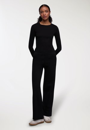 Maglietta nera a maniche lunghe abbinata a pantaloni neri a gamba larga. L'outfit presenta una consistenza liscia e una cintura elastica. Sneakers bianche casual completano il look.