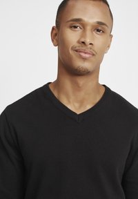 Black v-neck sweater made of knit fabric, featuring ribbed edges and a textured finish. Close-up view of the top portion with natural lighting.