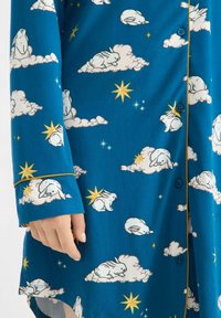 Modrá látka s opakujícím se vzorem bílých králíků na mracích a žlutých hvězdách. Obsahuje zapínání na knoflíky a kontrastní žluté lemování.